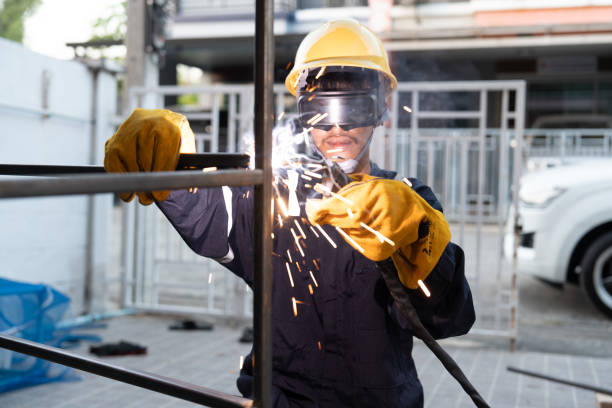 Asian worker wearing safety suit uses a welding machine. The sparking of the welding wire and steel creates sparks.